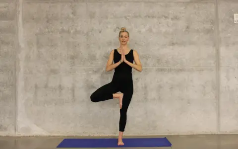 Kvinna i svart träningsklädsel utför trädpositionen, en klassisk yogaövning som passar utmärkt för senior yoga.