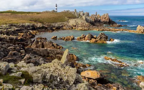 Phare noir et blanc sur une côte rocheuse et sauvage d'Ouessant. Combien de temps pour visiter Ouessant ? Une journée suffit pour admirer ce paysage.
