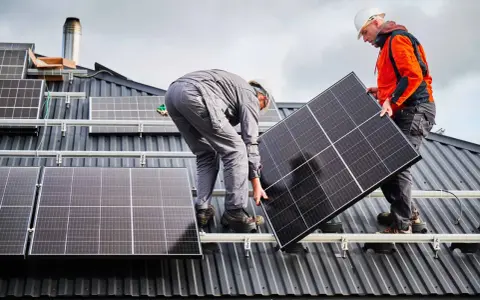 Deux ouvriers installent un panneau solaire sur un toit. La dimension du panneau solaire est adaptée pour maximiser la capture d'énergie.