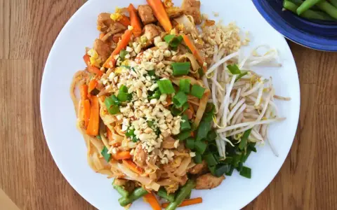 Pyszny sos pad thai z kurczakiem, warzywami i orzeszkami ziemnymi, podany z kiełkami fasoli mung.