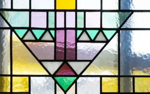 Un motif géométrique coloré orne cette fenêtre vitraux, mêlant le jaune vif, le violet doux et le vert émeraude.