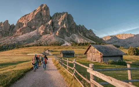 Piękna fotografia krajobrazowa Dolomitów. Grupa turystów wędruje ścieżką obok drewnianych chat, pod majestatycznymi szczytami górskimi.