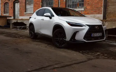 Biały Lexus 350h z czarnymi felgami stoi przed starą ceglaną budowką.