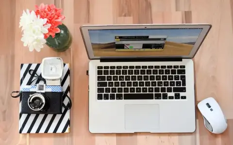 Jak zgrać zdjęcia z aparatu na laptop? Na biurku leży aparat, laptop i myszka.
