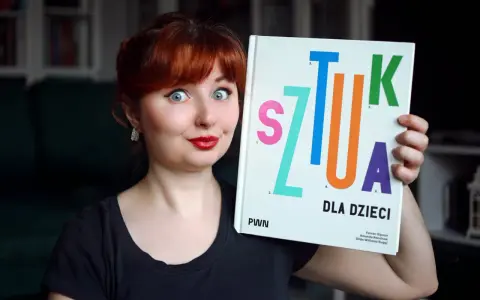 Kobieta z rudymi włosami trzyma książkę "Sztuka dla dzieci". Jej oczy są szeroko otwarte, a usta umalowane na czerwono.