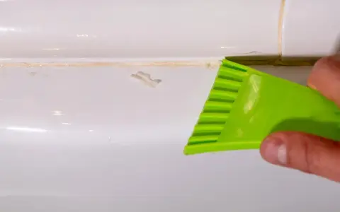 Outil vert raclant du mastic durci sur une surface blanche.