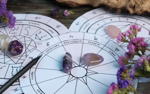 Astrologiczne koła zodiaku, kamienie, kostki i fioletowe kwiaty. 27 wrzesień znak zodiaku to Waga, symbolizująca równowagę.