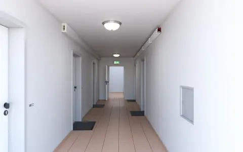 Ein langer, heller Flur mit mehreren Türen und einem grünen Notausgangsschild. Dieser notwendiger Flur ist gut beleuchtet und wirkt einladend.