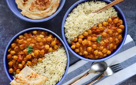 Dos tazones de curry de garbanzos con arroz basmati y pan naan.