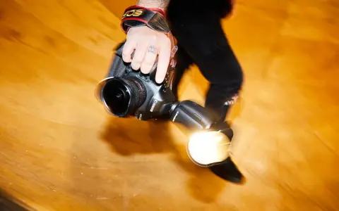Dłoń fotografa trzyma aparat z lampą błyskową. Długi czas naświetlania tworzy efekt ruchu.