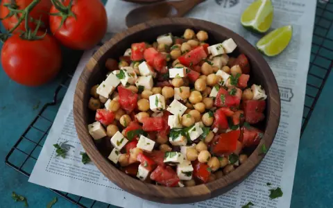 Ein köstlicher, **high protein salat** aus Kichererbsen, Tomaten und Feta in einer Holzschale, garniert mit Petersilie.