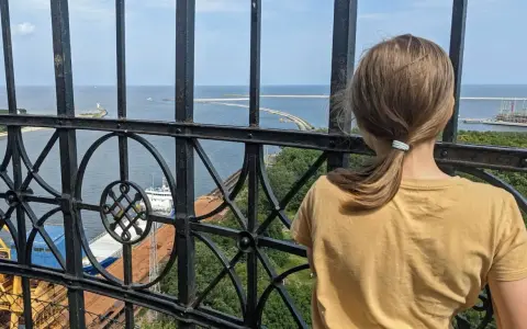 Dziewczynka podziwia widok z najwyższej latarni morskiej w Polsce. Widać morze, port i statki.