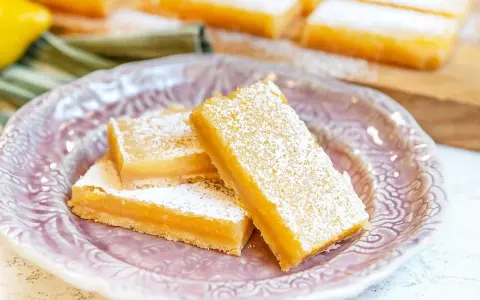 Citronkaka i långpanna, pudrad med florsocker, ligger upplagd på en vacker lila tallrik.