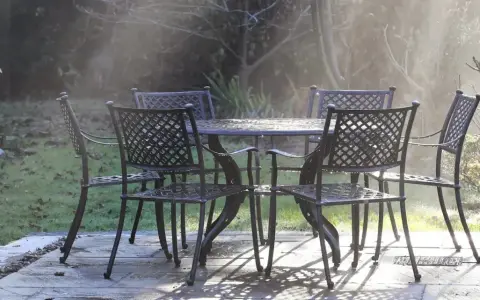 Un ensemble de mobilier de jardin résistant aux intempéries, une table et quatre chaises en métal, est mouillé par la rosée matinale.