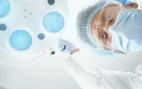 Chirurg w masce i okularach pochyla się nad pacjentem, przygotowując zalecenia po operacji prostaty.