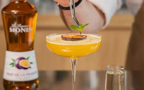 Barman dekoruje drink likierem z marakui, dodając listek mięty. Obok stoi butelka Monin.