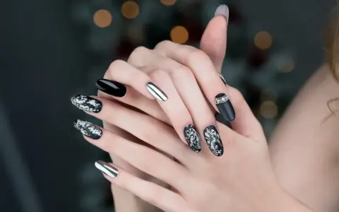 Mani con unghie particolari: nero lucido, argento specchiato e decorazioni floreali in bianco e argento con strass.