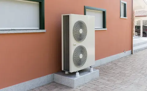 Unité extérieure d'une pompe à chaleur, installée sur un socle devant un mur de maison. Ce système contribue à réduire le cout aerothermie.