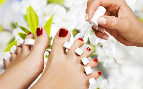 Malowanie paznokci u stóp na czerwono to kluczowy etap, jak zrobić pedicure. Dłonie z lakierem i separatorami między palcami.