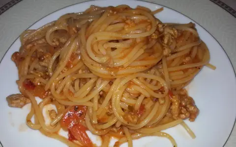 Pyszne spaghetti bolognese z passaty, z mielonym mięsem i kawałkami pomidorów, podane na białym talerzu.