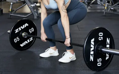 Donna in palestra si prepara per gli stacchi da terra con un bilanciere.