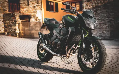 Czarny motocykl Kawasaki na brukowanej ulicy, z budynkami w tle.