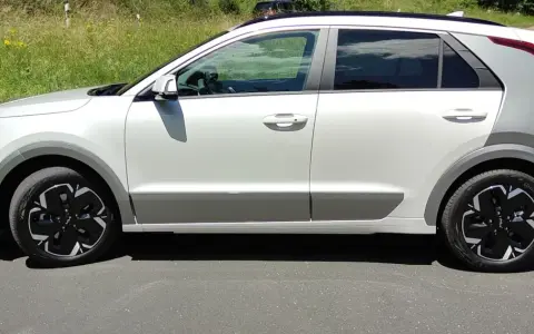 Biały Kia Niro EV z czarnymi felgami stoi na drodze, otoczony zielenią.