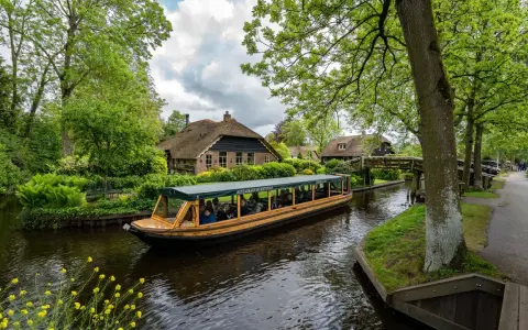 Bootfahrt durch Giethoorn, das Venedig der Niederlande. Grüne Ufer, Reetdachhäuser und gelbe Blumen am Wasser.