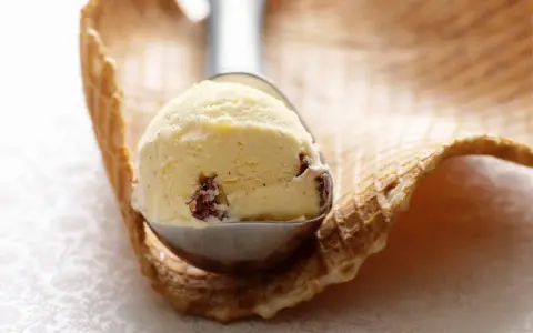 Ein Löffel cremiges Eis mit Rosinen und einem Hauch Rum ruht auf einem Waffelrand.