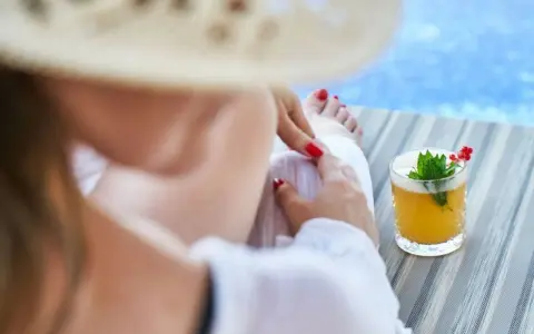 Relaks przy basenie z drinkiem w hotelu dla dorosłych Polska. Kobieta w słomkowym kapeluszu odpoczywa na leżaku.