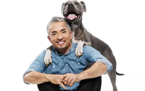 Cesar Millan z uśmiechniętym psem, który kładzie mu łapy na ramionach.