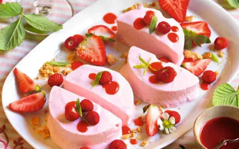Delizioso semifreddo alle fragole, guarnito con fragoline di bosco, salsa rossa e foglioline verdi.