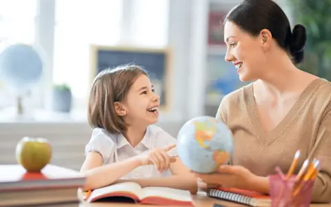 Niña y maestra sonríen mientras exploran un globo terráqueo. Un ejemplo de como ser un buen profesor, inspirando curiosidad y aprendizaje.