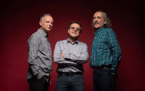 Los miembros de Els Pets posan sonrientes ante un fondo rojo.