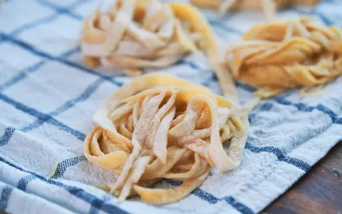 Świeże, domowe tagliatelle lub makaron spaghetti ułożone na lnianym ręczniku w kratkę.