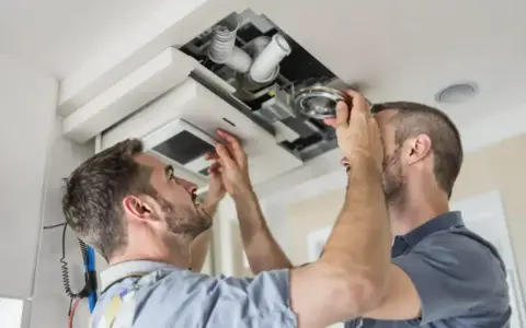 Deux hommes installent un système VMC dans un faux plafond. C'est là où se trouve la VMC dans une maison.