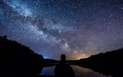 Zachwycająca fotografia astronomiczna Drogi Mlecznej nad jeziorem. Sylwetka człowieka kontempluje kosmos.