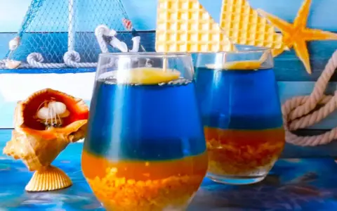 Dwa orzeźwiające drinki Błękitna Laguna, ozdobione plasterkiem cytryny, na tle morskich dekoracji.