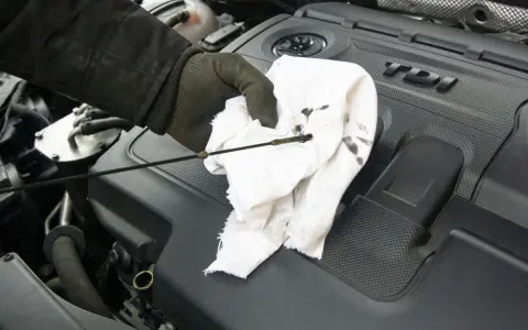Ręka w rękawiczce wyciera bagnet z ciemnymi śladami zużytego oleju silnikowego na tle czarnej pokrywy silnika TDI.