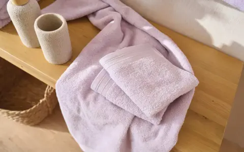 Variedad de tipos de toallas de baño en color lavanda, apiladas sobre una superficie de madera.