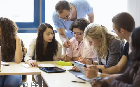 Des étudiants travaillent en groupe, un enseignant les supervise. Ils préparent leur diplôme BAFD, concentrés sur leurs notes et tablettes.