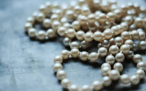 Collana di perle su sfondo grigio. Scopri come pulire la madreperla per mantenerla splendente.