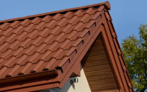 Brązowa, lekka konstrukcja dachu z dachówki ceramicznej, z widocznym okapem i drewnianą podbitką.