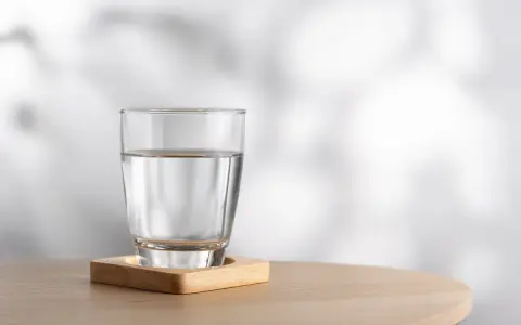 Szklanka czystej wody na drewnianej podstawce. Woda nie ma kalorii, to idealny napój dla zdrowia.