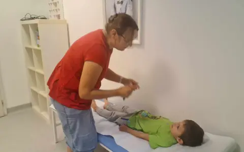Lekarz bada chłopca leżącego na kozetce, oceniając objawy uszkodzonego układu nerwowego u dziecka.