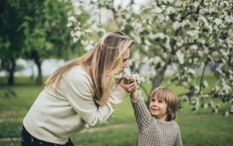Matka i dziecko w kwitnącym sadzie. Dziecko podaje mamie kwiatki, jakby ilustrowało przysłowia o miesiącach.