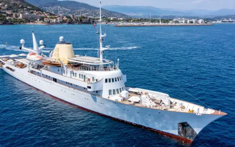 Die Christina O., eine luxuriöse Yacht, gleitet auf dem azurblauen Meer vor einer Küstenstadt.