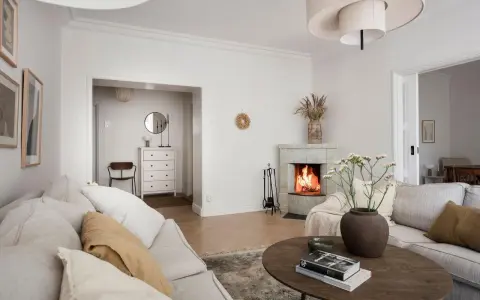 Accogliente soggiorno con camino acceso, divani chiari e un tavolino in legno. Idee per la casa e la campagna.
