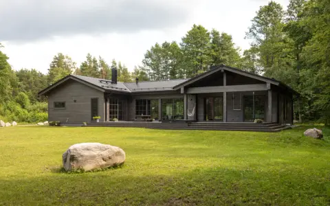 Ein modernes Architektenhaus aus Holz, eingebettet in üppiges Grün. Große Fensterfronten und eine Terrasse laden zum Entspannen ein.