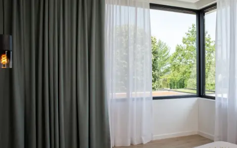 Cortinas bandalux grises y blancas en un dormitorio moderno, con vistas a un jardín frondoso.